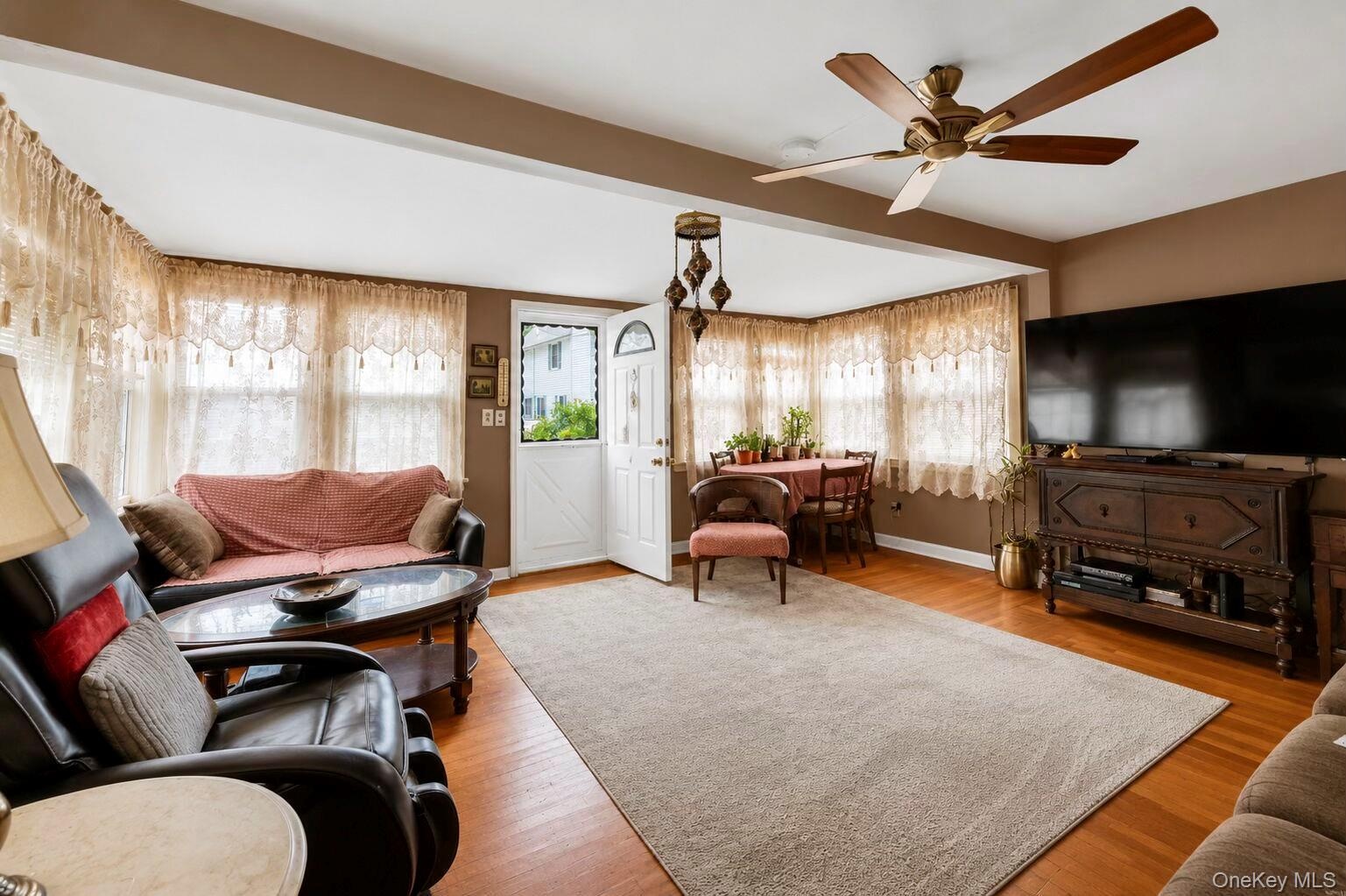 Spacious living area featuring wood-finish flooring, a ceiling fan with integrated lighting, and multiple windows