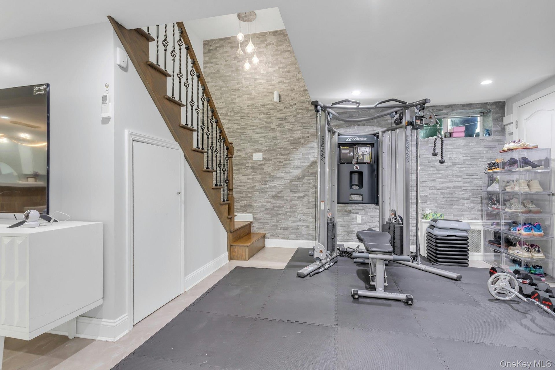 Finished lower level featuring a full staircase with wood treads and decorative iron balusters, stone accent walls, recessed lighting with lots of sto
