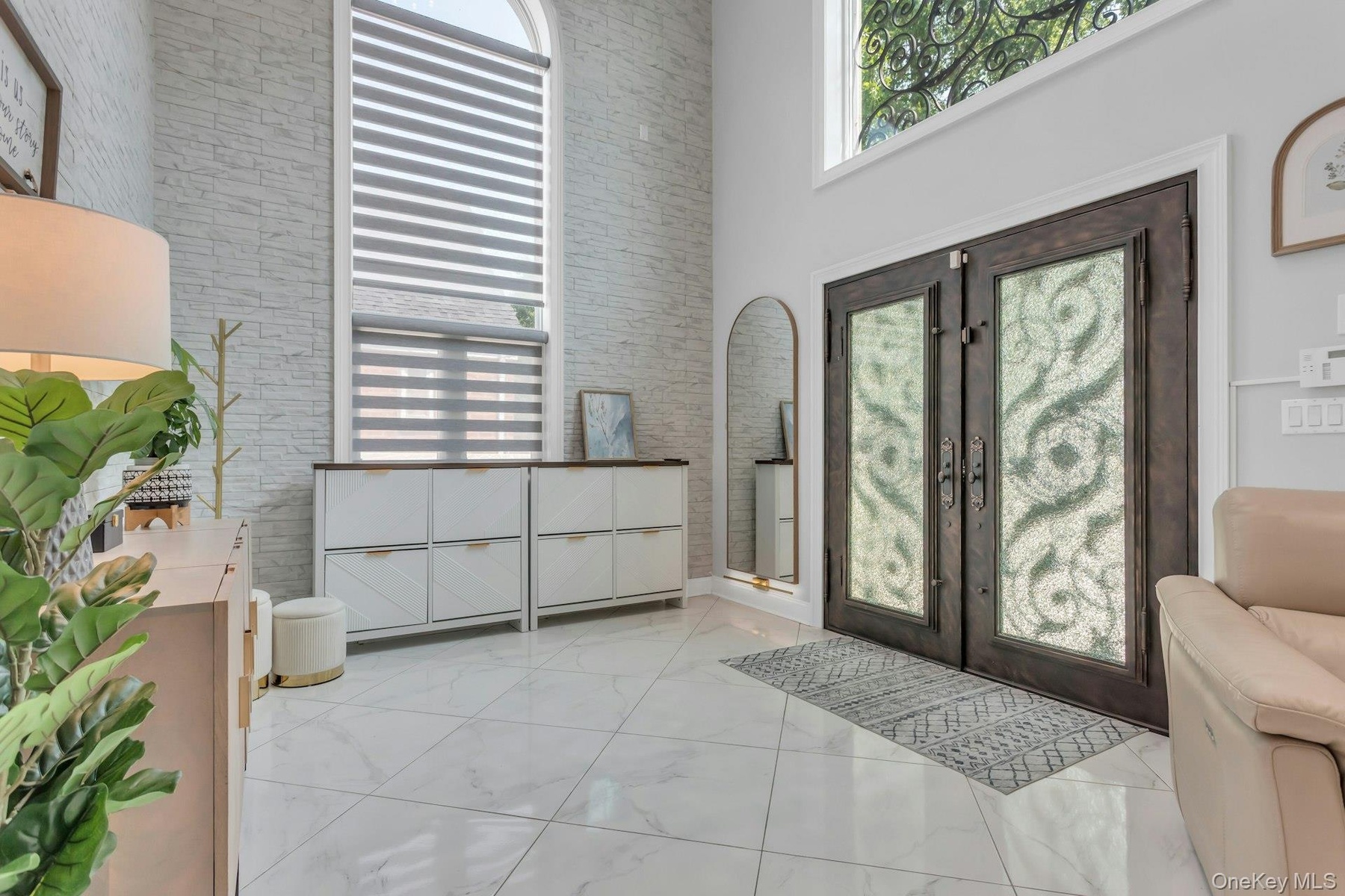 Double iron entry doors featuring crushed glass panels, stacked stone accent wall, over-sized elliptical windows providing a warm ambiance of light, e