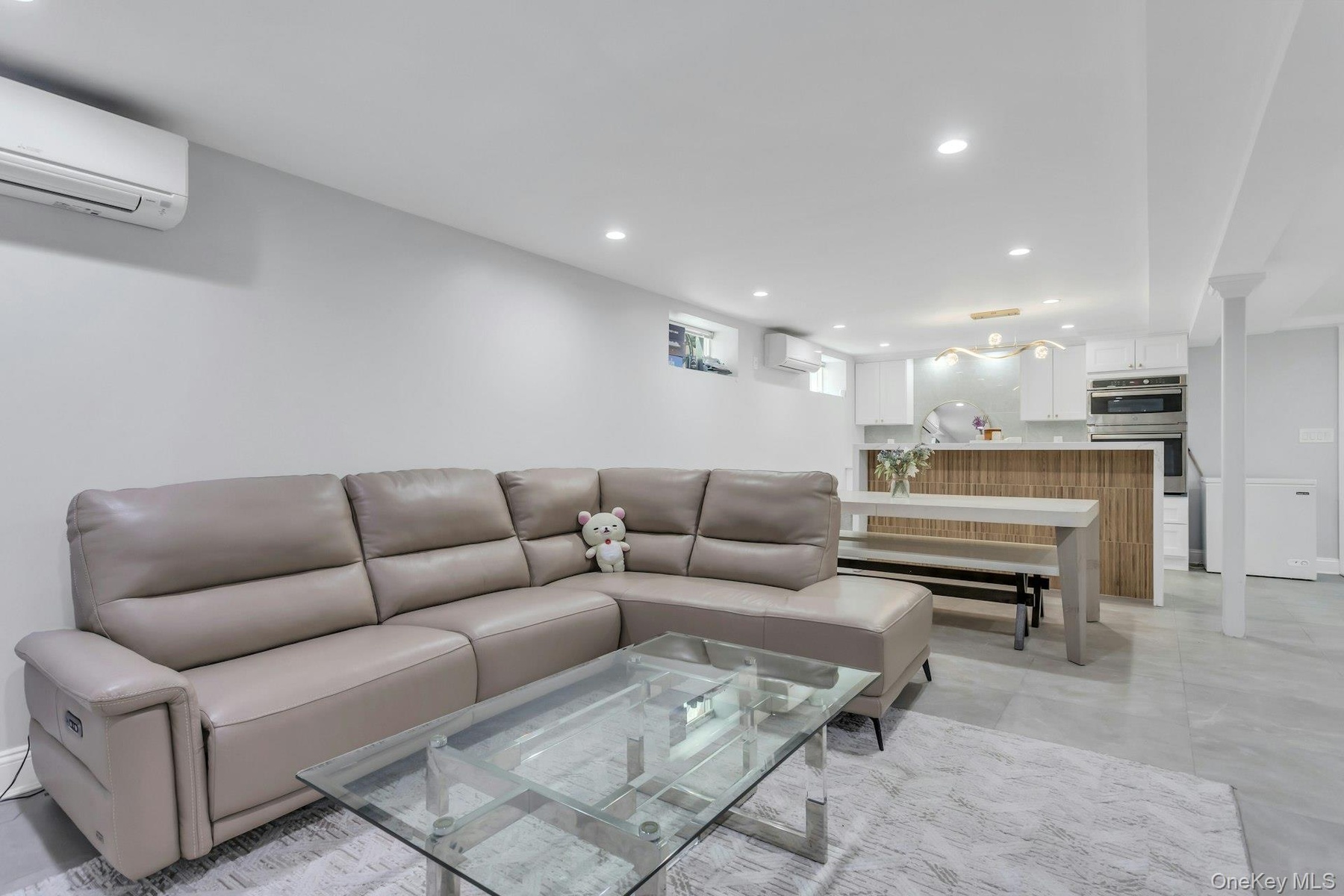 Lower level Open-concept living area featuring light gray walls, recessed lighting, and large format tile flooring