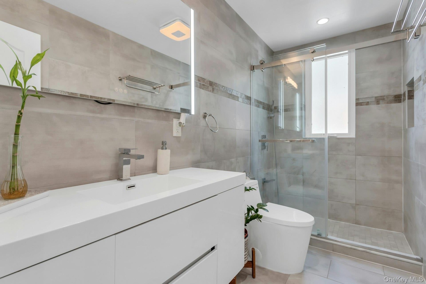 Contemporary bathroom featuring a floating white vanity with integrated sink, chrome faucet, and an illuminated mirror