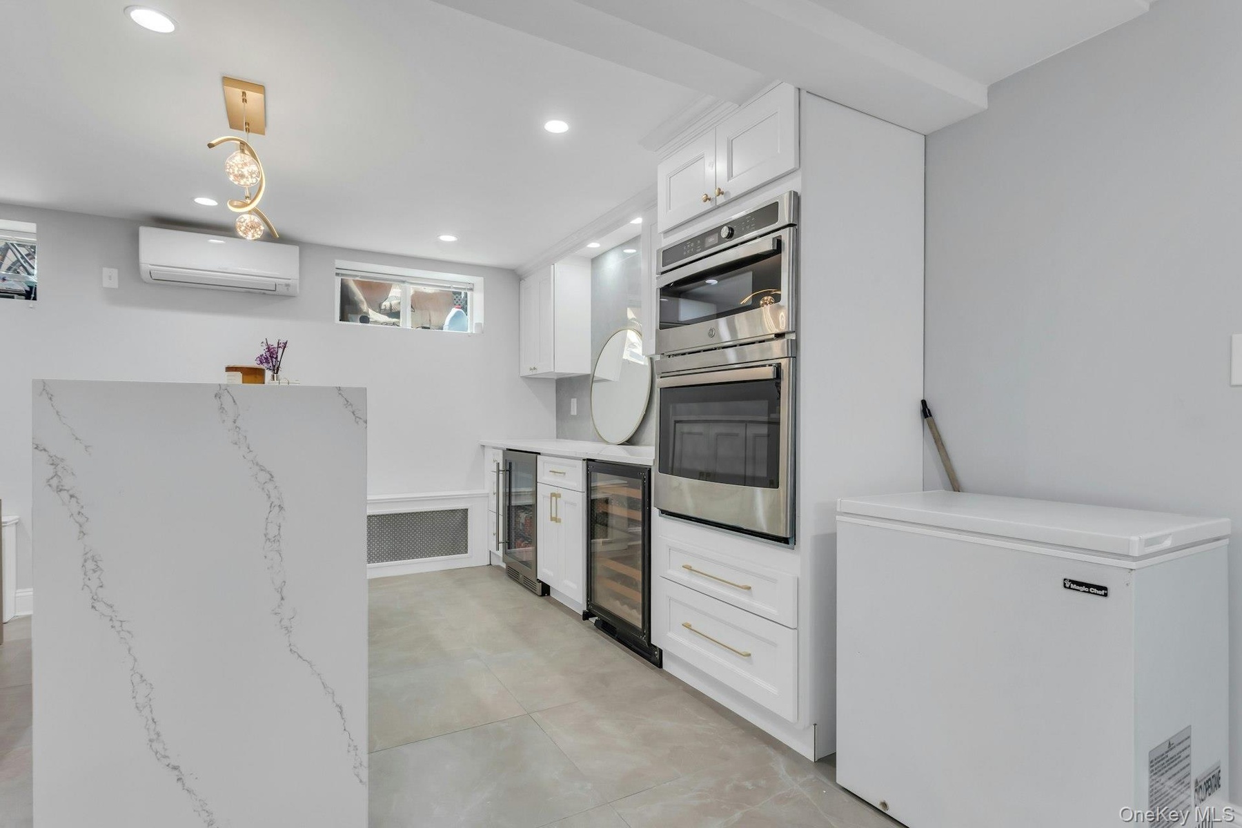 Bonus: Contemporary kitchen space featuring a waterfall island with veined quartz, recessed lighting, and a gold-tone linear chandelier