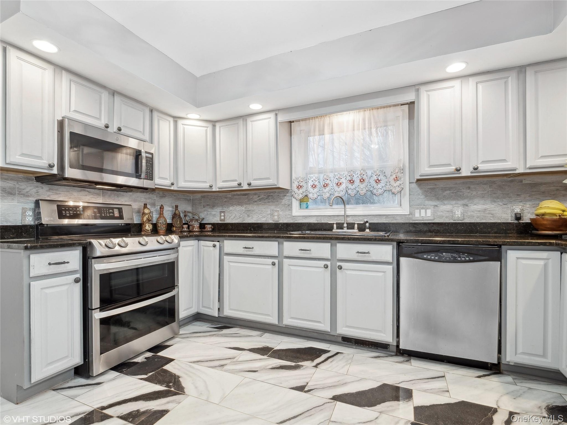 Kitchen with decorative backsplash, white cabinetry, sink, and stainless steel appliances