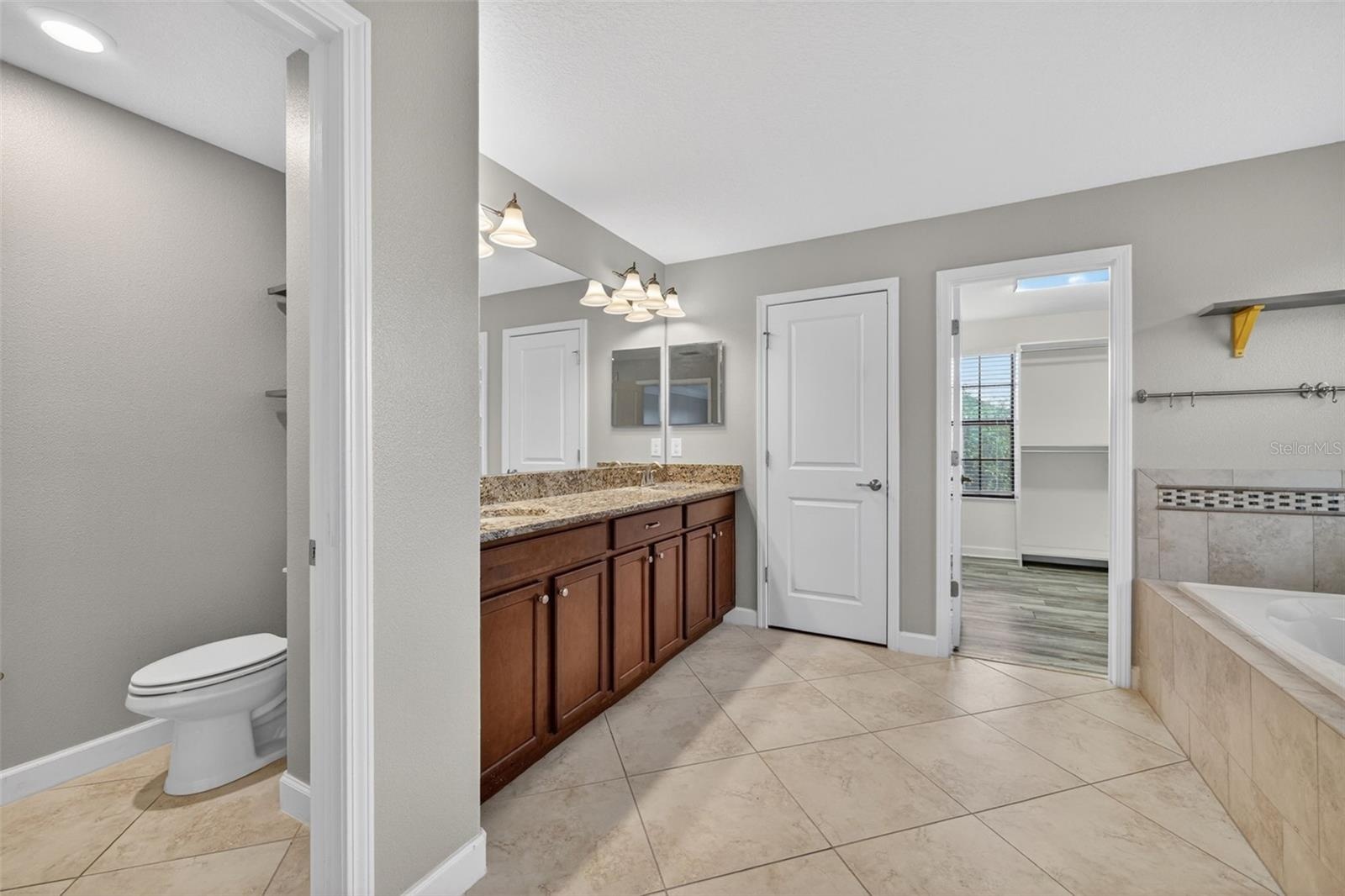 Primary En-Suite Bathroom with Dual Vanities, Granite Countertops, Garden Soaking Tub with Window, Shower Stall with Glass Frame, Private Water Closet