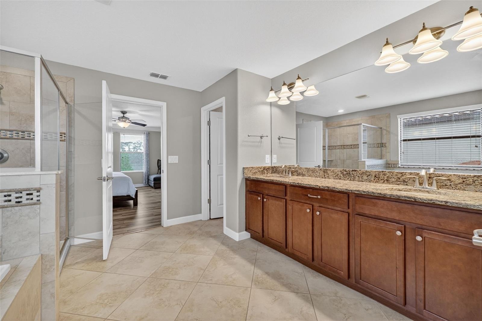 Primary En-Suite Bathroom with Dual Vanities, Granite Countertops, Garden Soaking Tub, Shower Stall with Glass Frame, Private Water Closet, Linen Clos