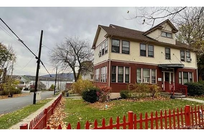 Three-story residence featuring a prominent dormer, a red picket fence, and a front entrance with a covered porch and red railings