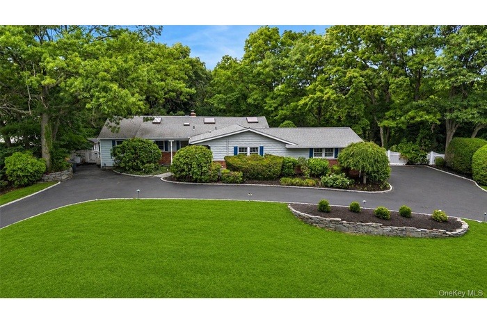 Ranch-style residence featuring light blue siding with blue window shutters, set against a backdrop of mature trees. Front Lawn enchanced with color c