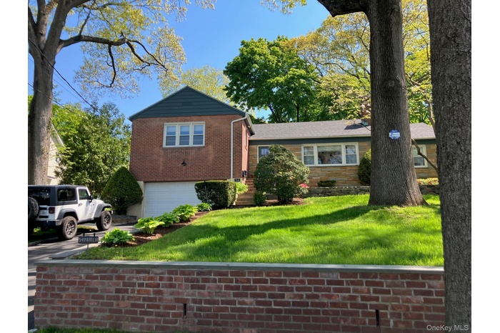 Split-level residence featuring a brick and stone facade, attached garage, and a sloped, manicured lawn