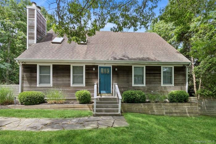 Shingle-sided residence featuring a prominent chimney, an entryway with steps and railings, and a blue door