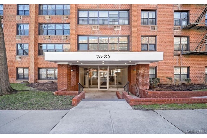 Brick facade building featuring multiple large windows, a recessed entrance, and a canopy with building numbers