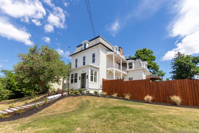 White multi-story residence featuring a mansard roof, dormer windows, and a front porch