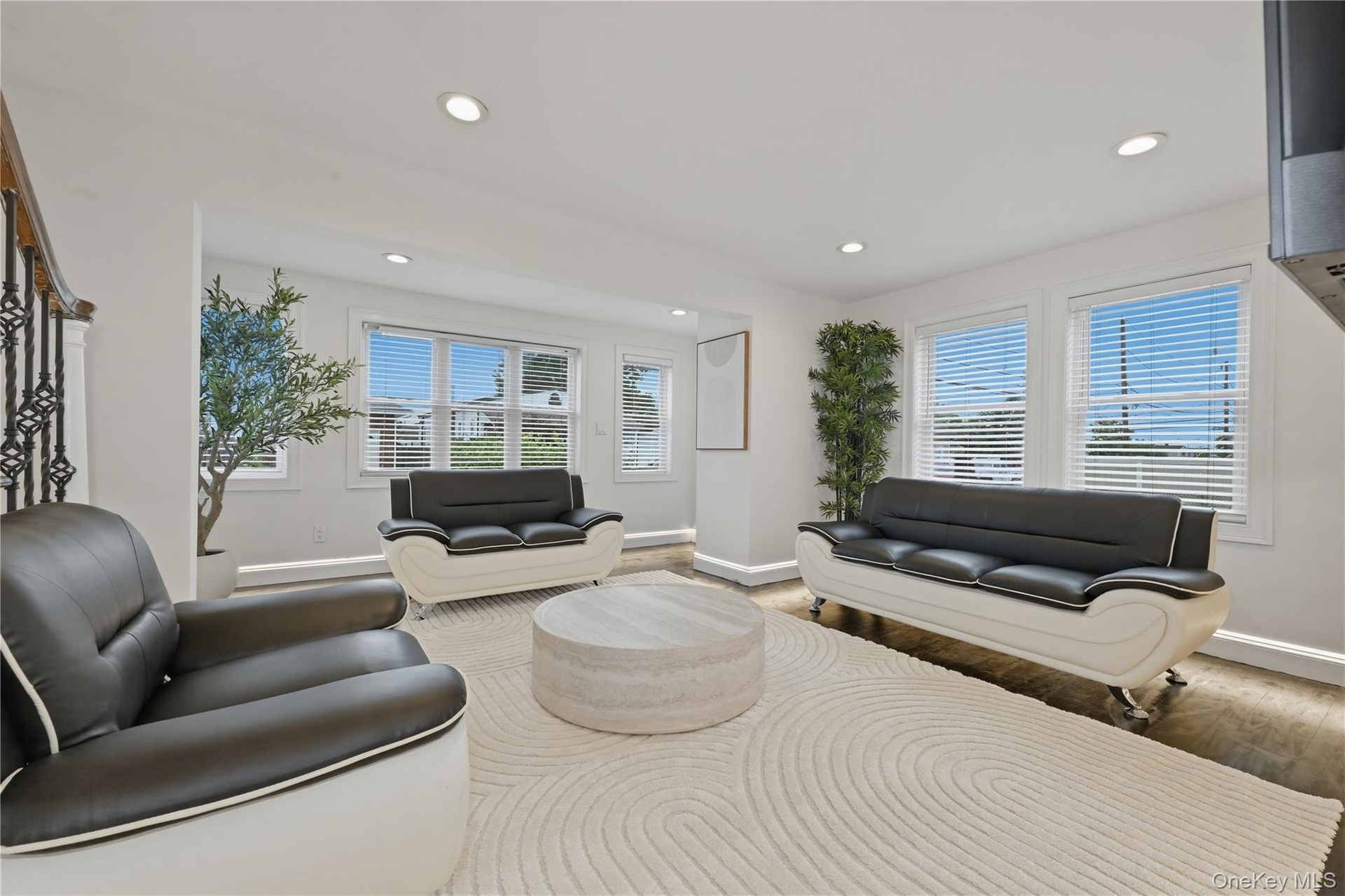 Bright interior space featuring recessed lighting, multiple windows with blinds, wood-finish flooring, and a decorative wrought iron staircase railing
