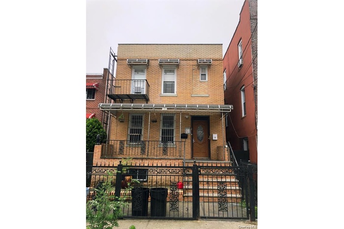 Brick facade building featuring a wrought iron fence, security bars on windows, a ground-level patio, and a second-story balcony