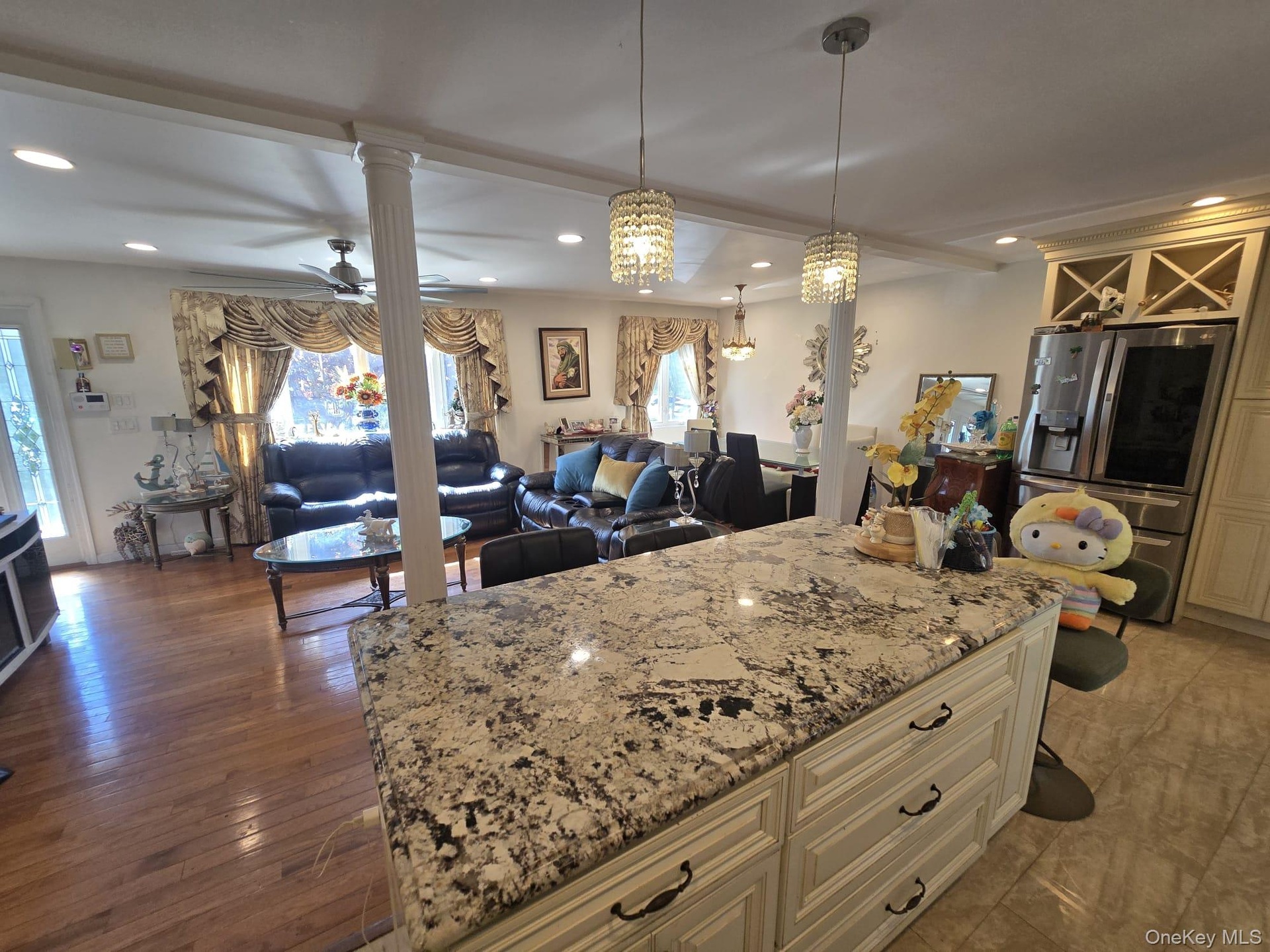 Spacious open-concept interior featuring a large kitchen island with a speckled countertop and cream-colored cabinetry, two crystal pendant lights, re