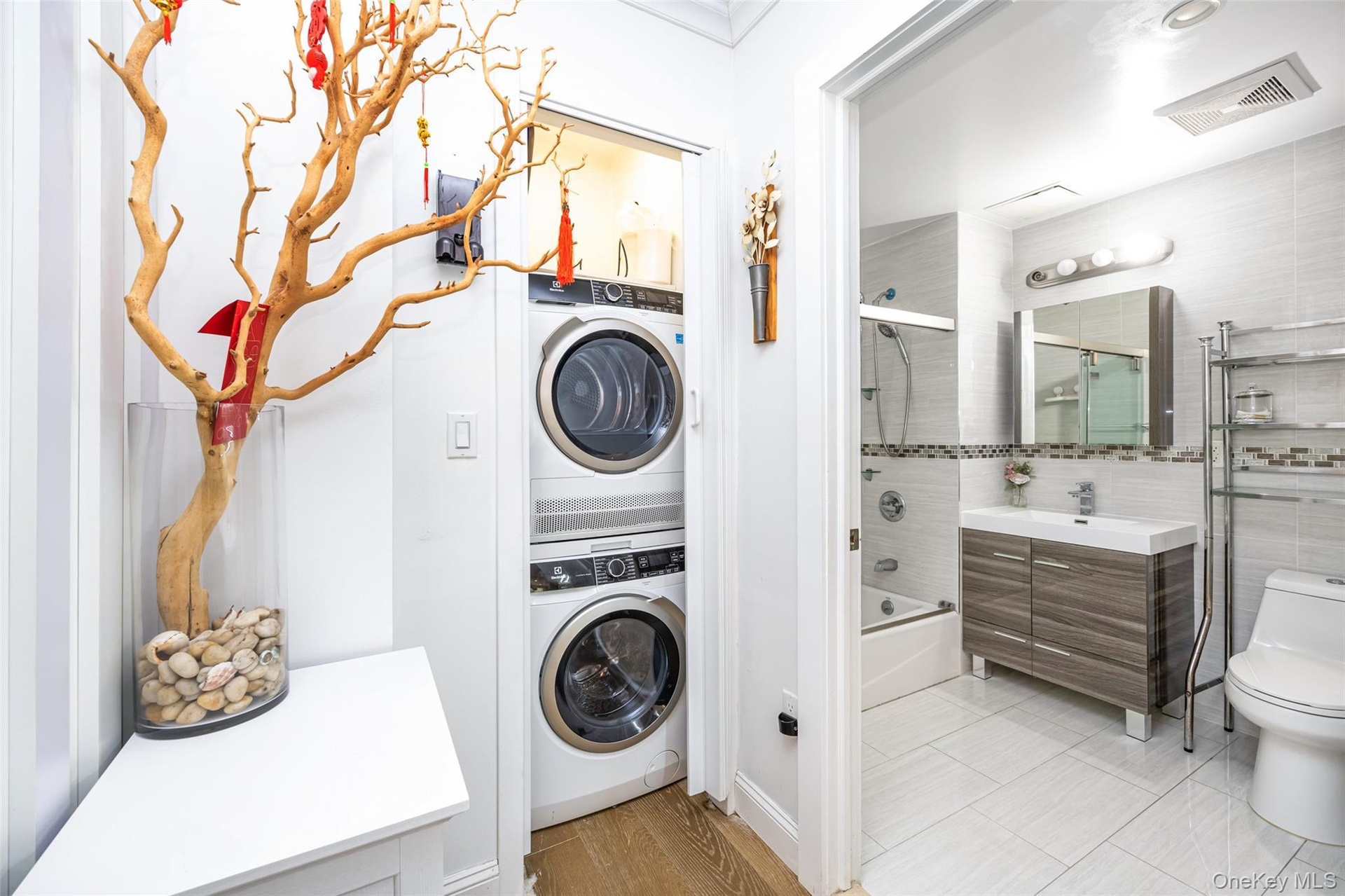 Laundry room with stacked washing machine and dryer and light wood-type flooring