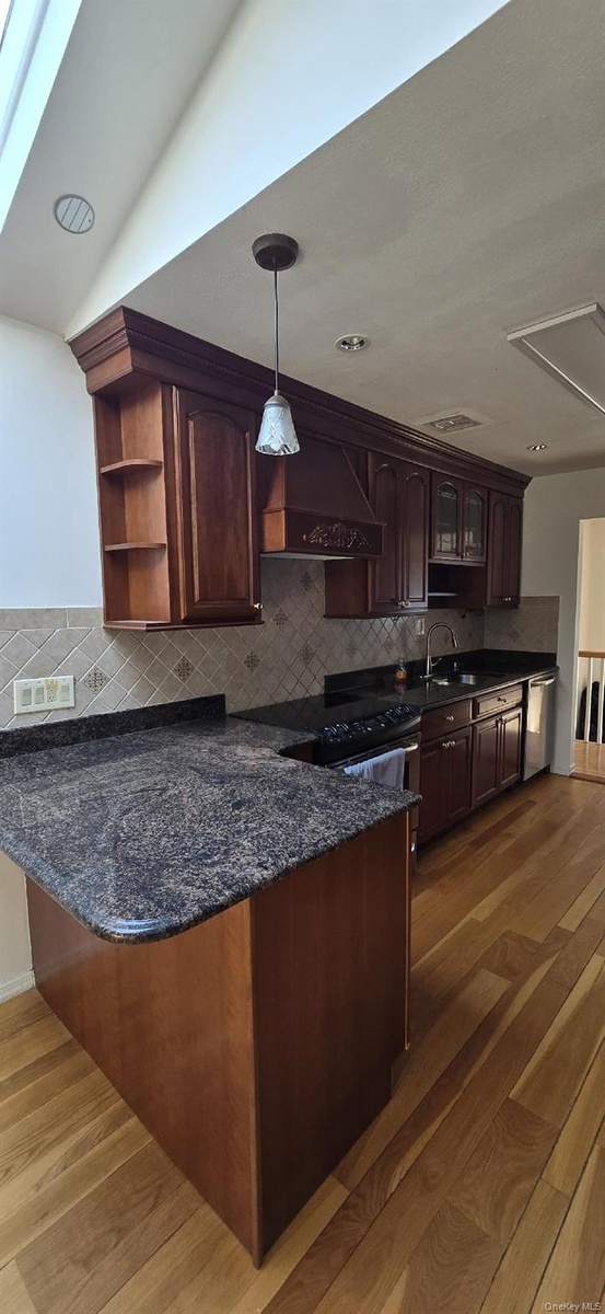 Kitchen featuring rich wood cabinetry, patterned tile backsplash, dark stone countertops, stainless steel appliances, and wood-finish flooring