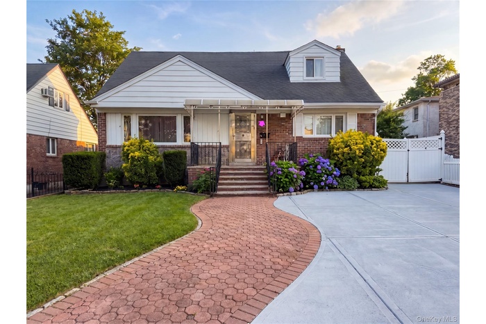 Brick and siding residence featuring a red paver walkway, mature landscaping, and a concrete driveway with a white privacy gate