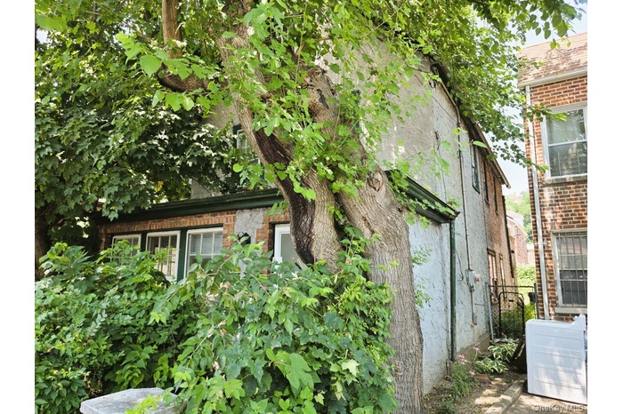 Exterior featuring mature trees, a stucco facade, brick accents, and white-framed windows with dark green trim