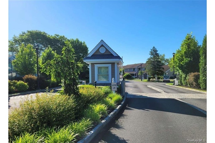 Entry gatehouse featuring a shingle roof and siding, surrounded by mature landscaping and paved roadways