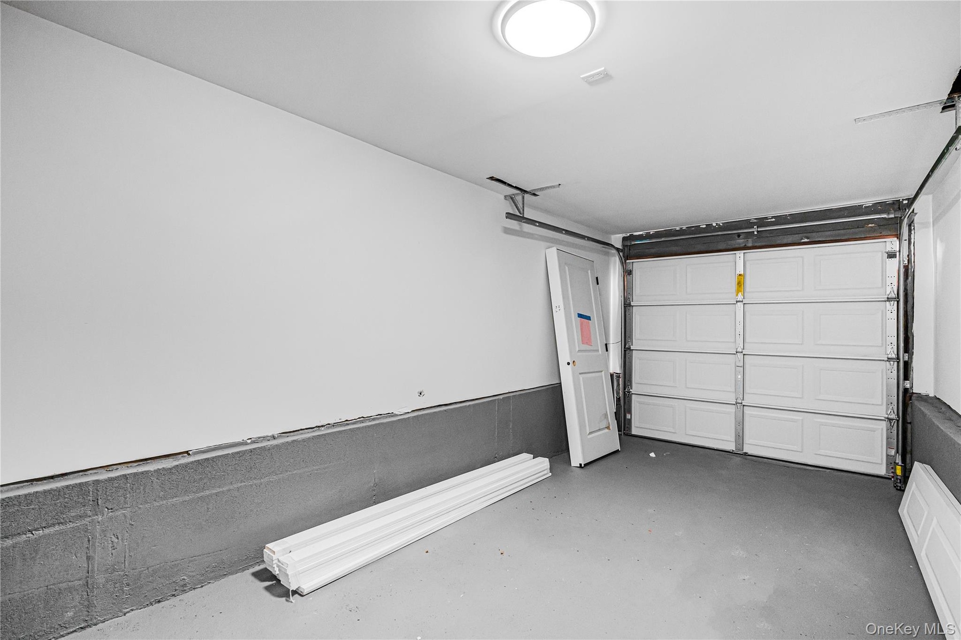 Garage interior featuring a white paneled door, gray concrete flooring, and a flush-mount ceiling light