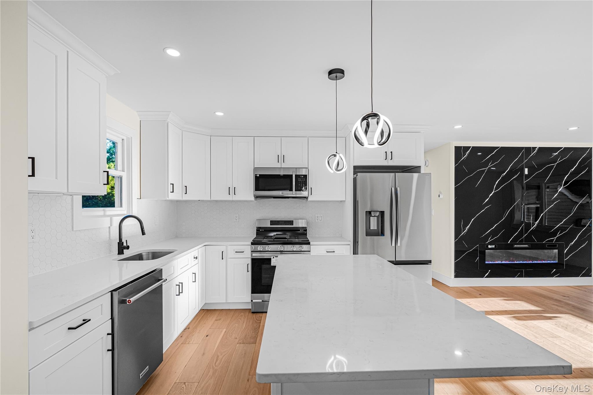 Kitchen featuring a central island with a light-toned countertop, white cabinetry with black hardware, stainless steel appliances, and a white tiled b