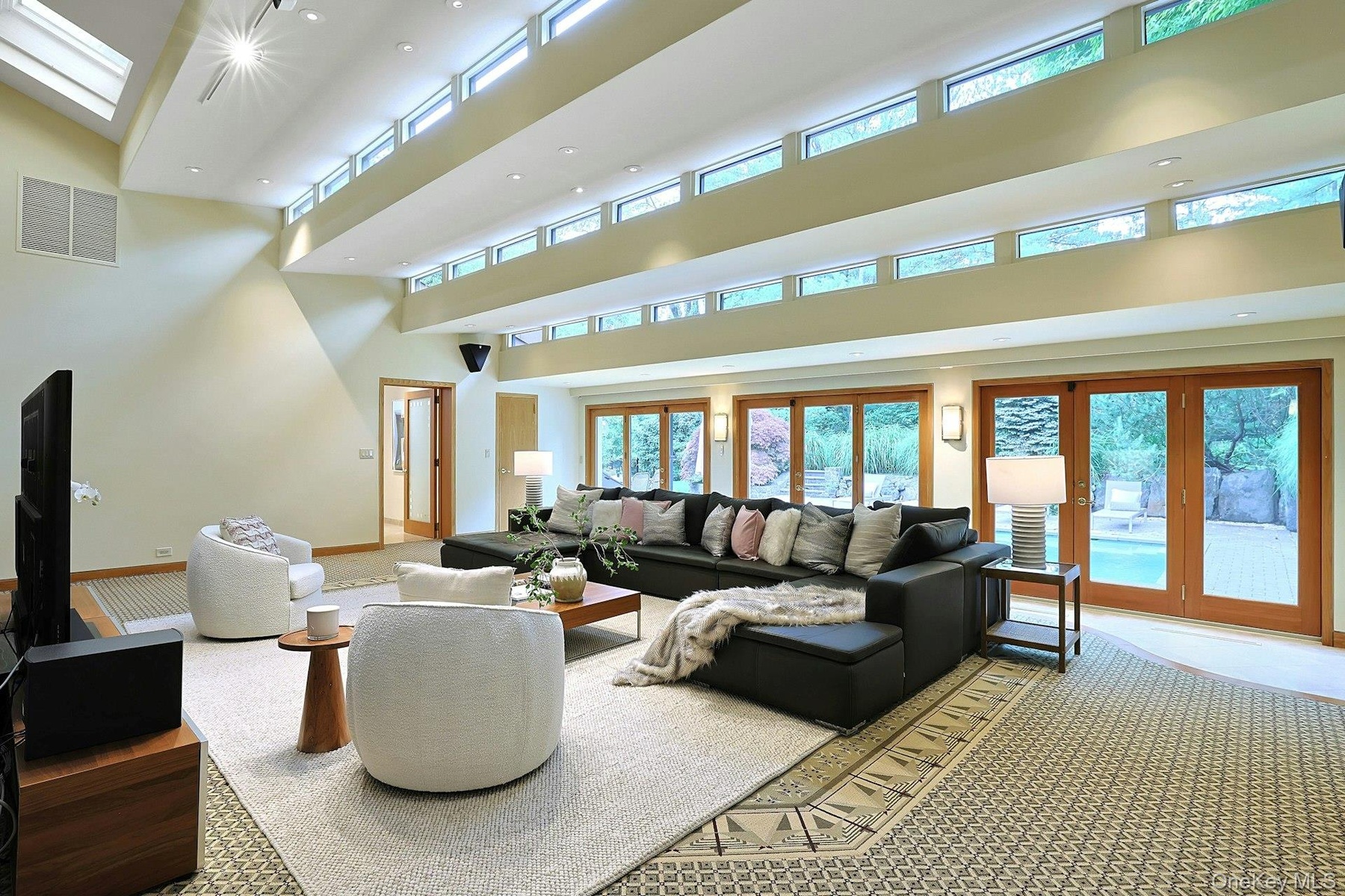 The extraordinary double-height family room showcases soaring ceilings, walls of glass, and seamless indoor-outdoor living.