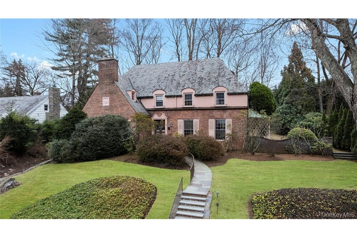 View of front of property featuring a chimney, a high end roof, stucco siding, brick siding, and a front yard