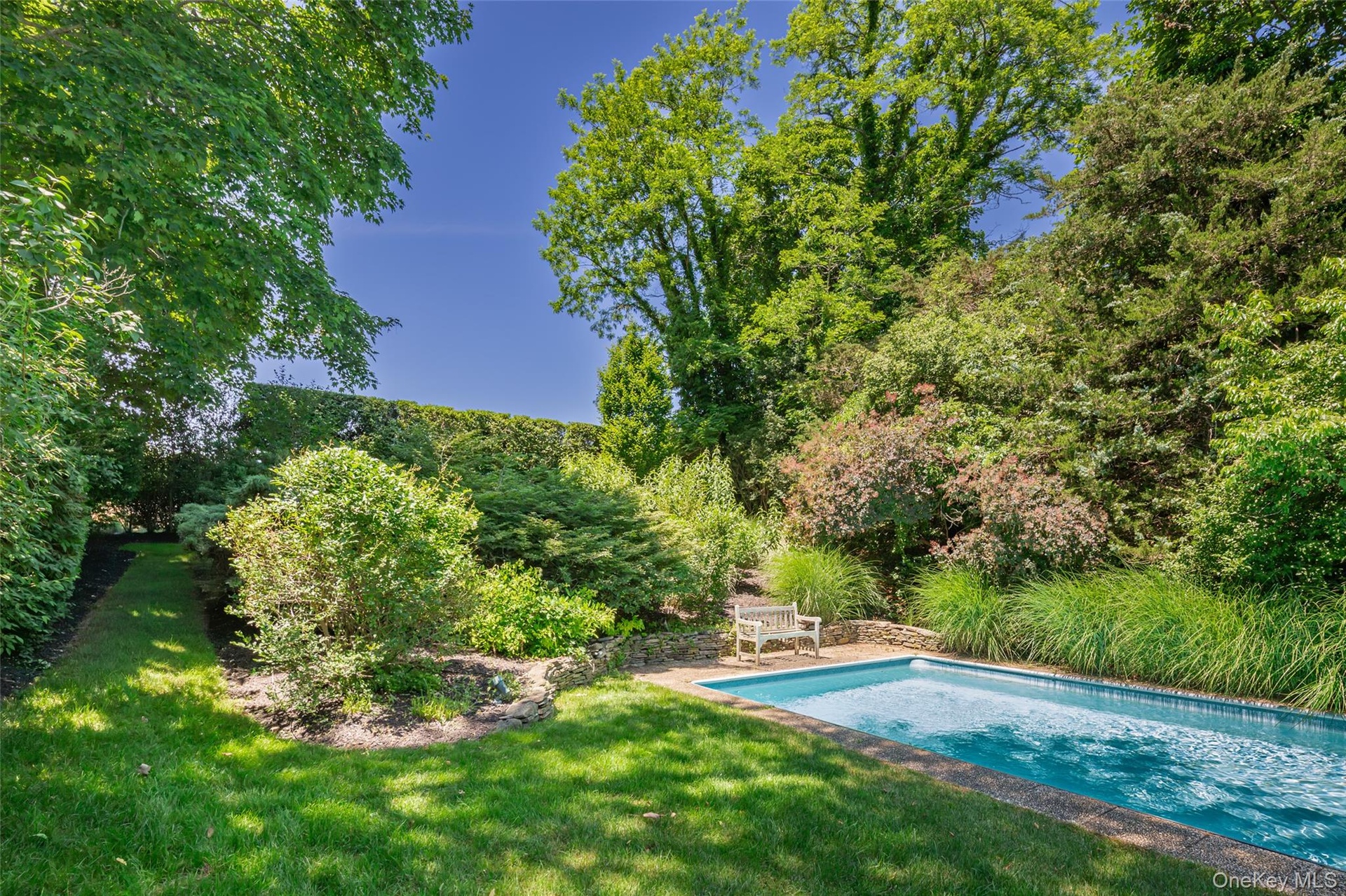 Rectangular in-ground swimming pool with stone coping and surrounding lawn