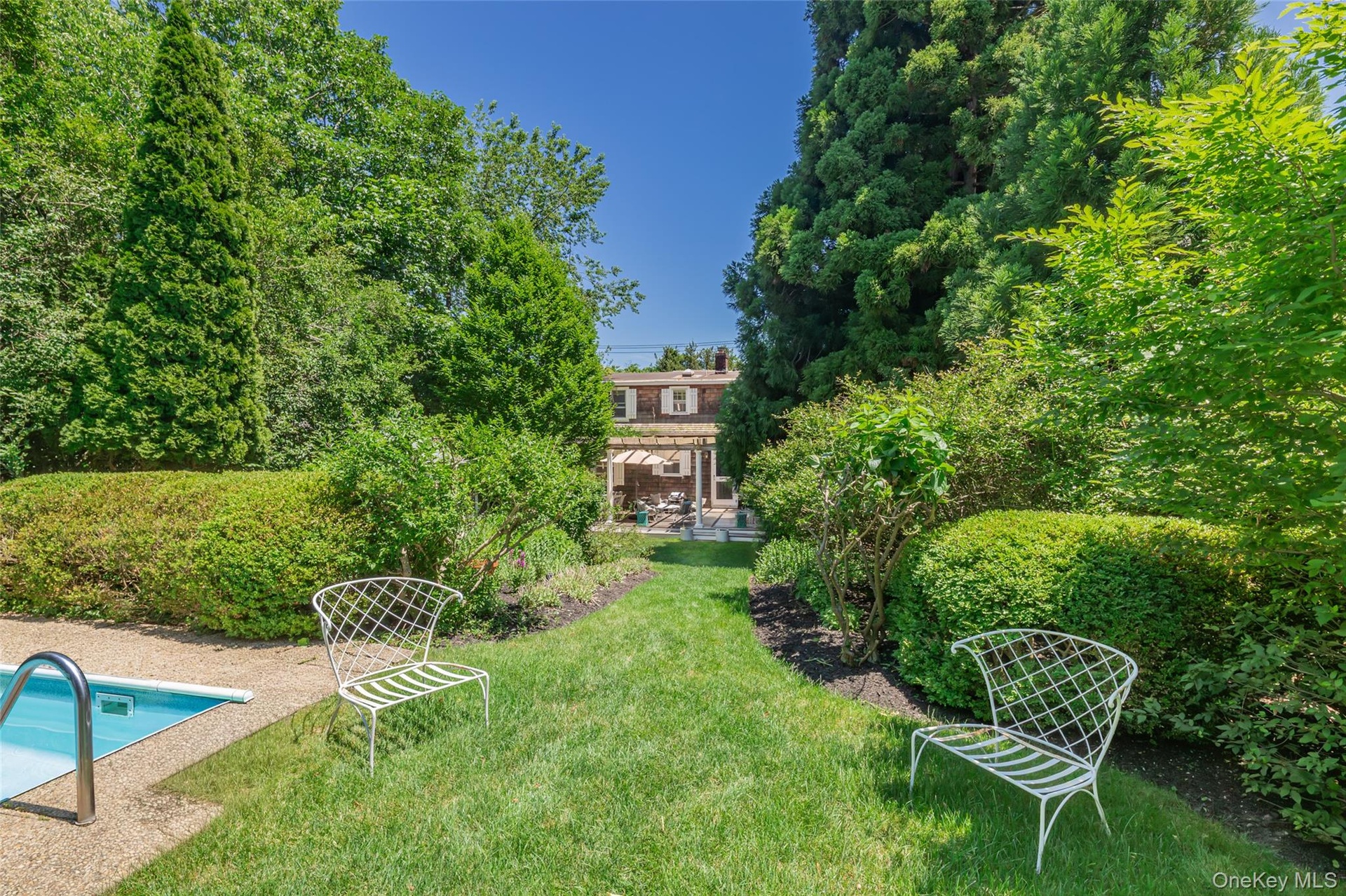 Expansive backyard featuring a manicured lawn, established shrubbery, and mature trees