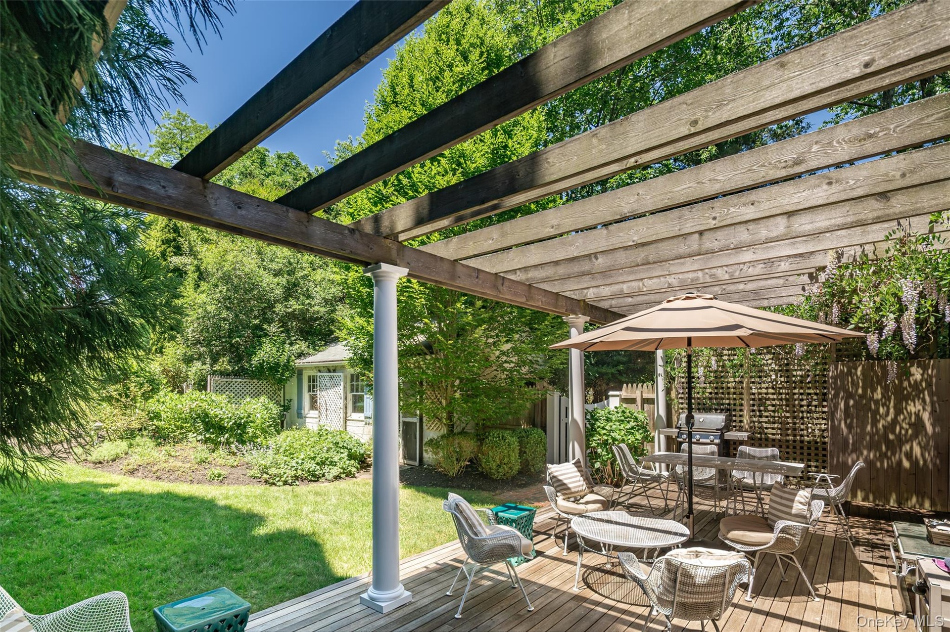 Expansive backyard featuring a wood deck with a pergola, a manicured lawn, and mature trees