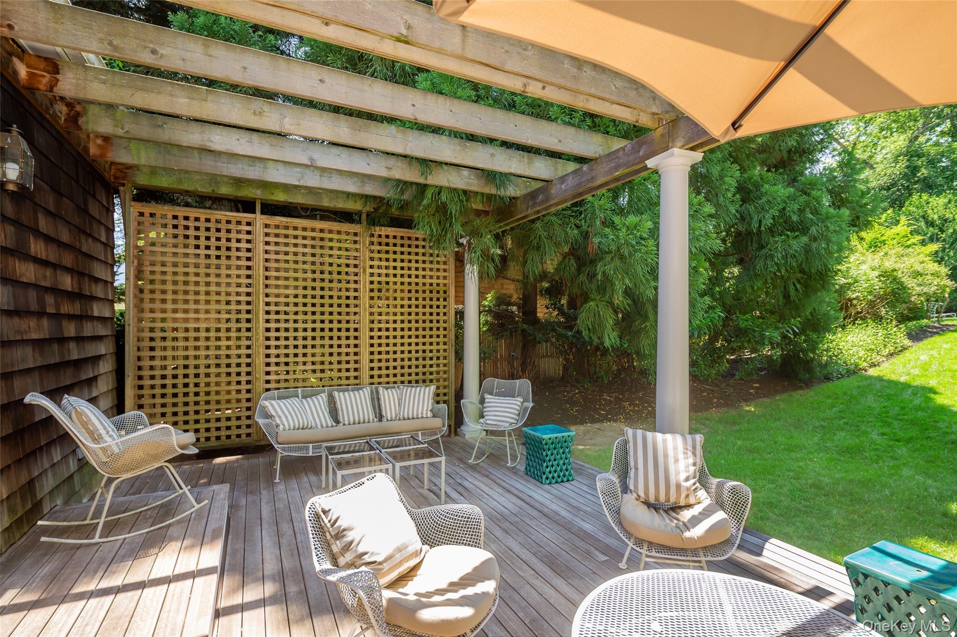 Spacious outdoor deck featuring natural wood flooring, a slatted pergola, a decorative privacy screen, a column support, and an attached umbrella for 