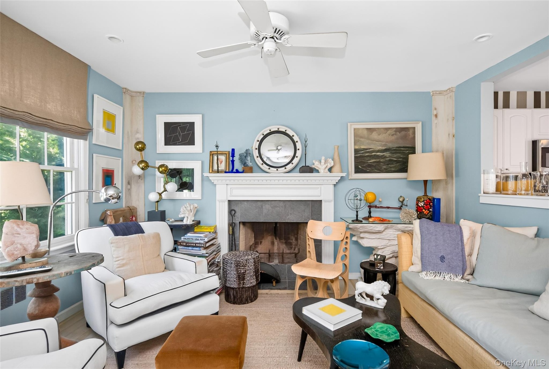 Living area featuring a white ceiling fan, light blue walls, and a fireplace with a white mantel and stone surround