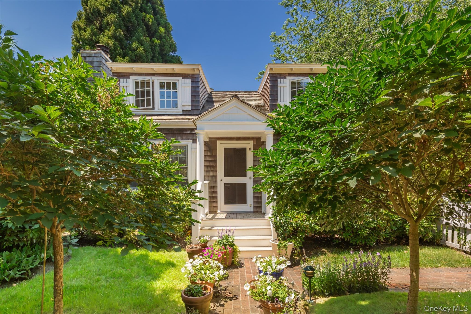 Shingle-style cottage featuring a gabled entry, white trim, and multi-pane windows with decorative shutters