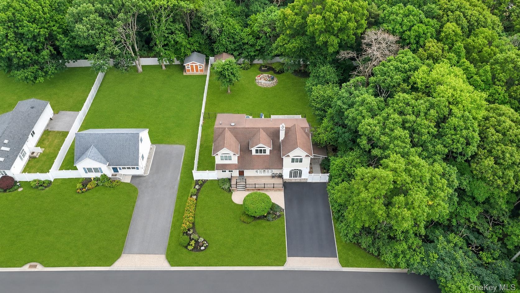 Expansive property featuring a multi-level residence with a brown shingle roof and white siding, an attached paved driveway, and a manicured lawn