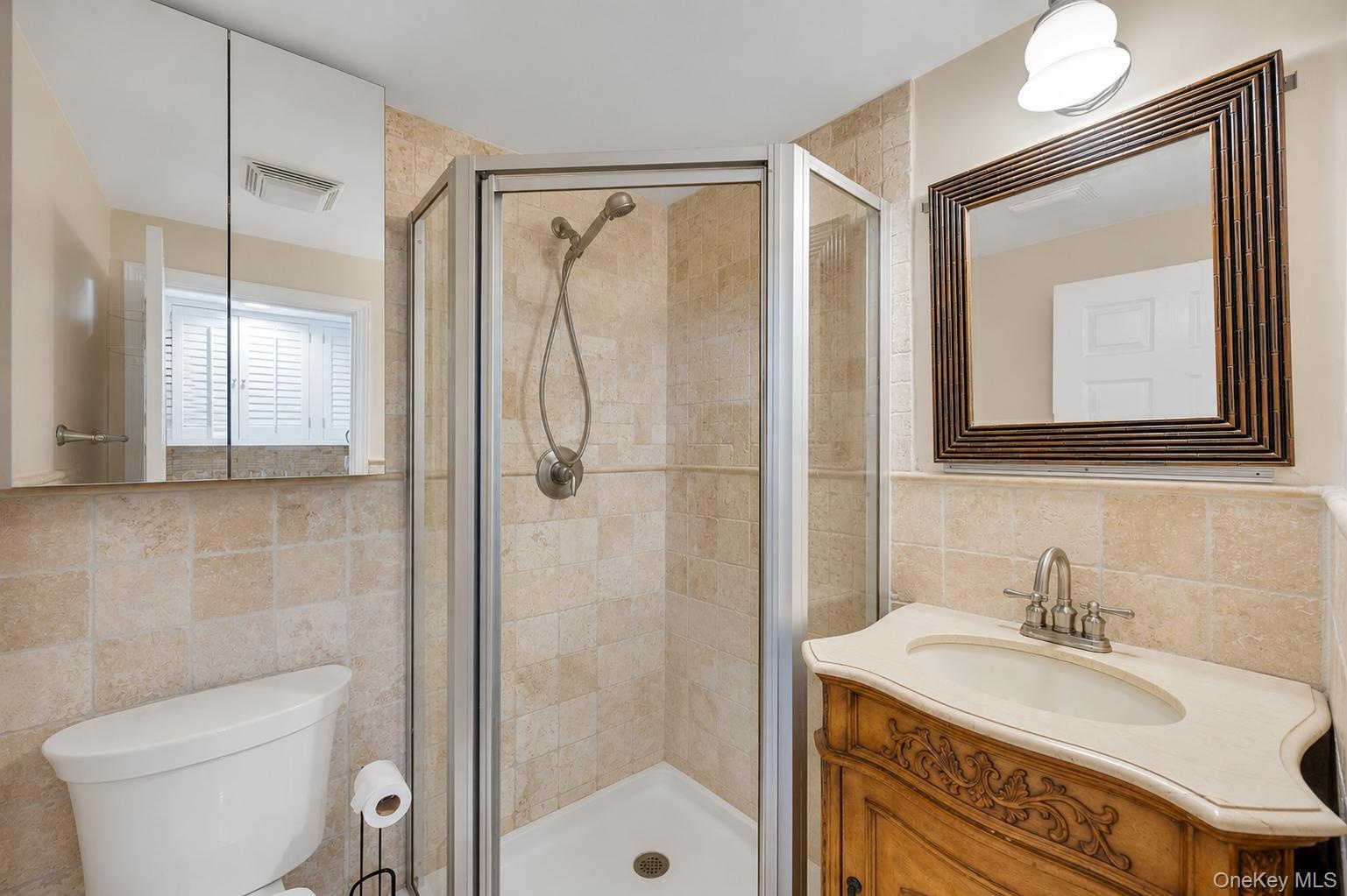 Bathroom featuring a corner shower with a glass enclosure, a vanity with an ornate wood-finish base and light-colored countertop, and a decorative fra