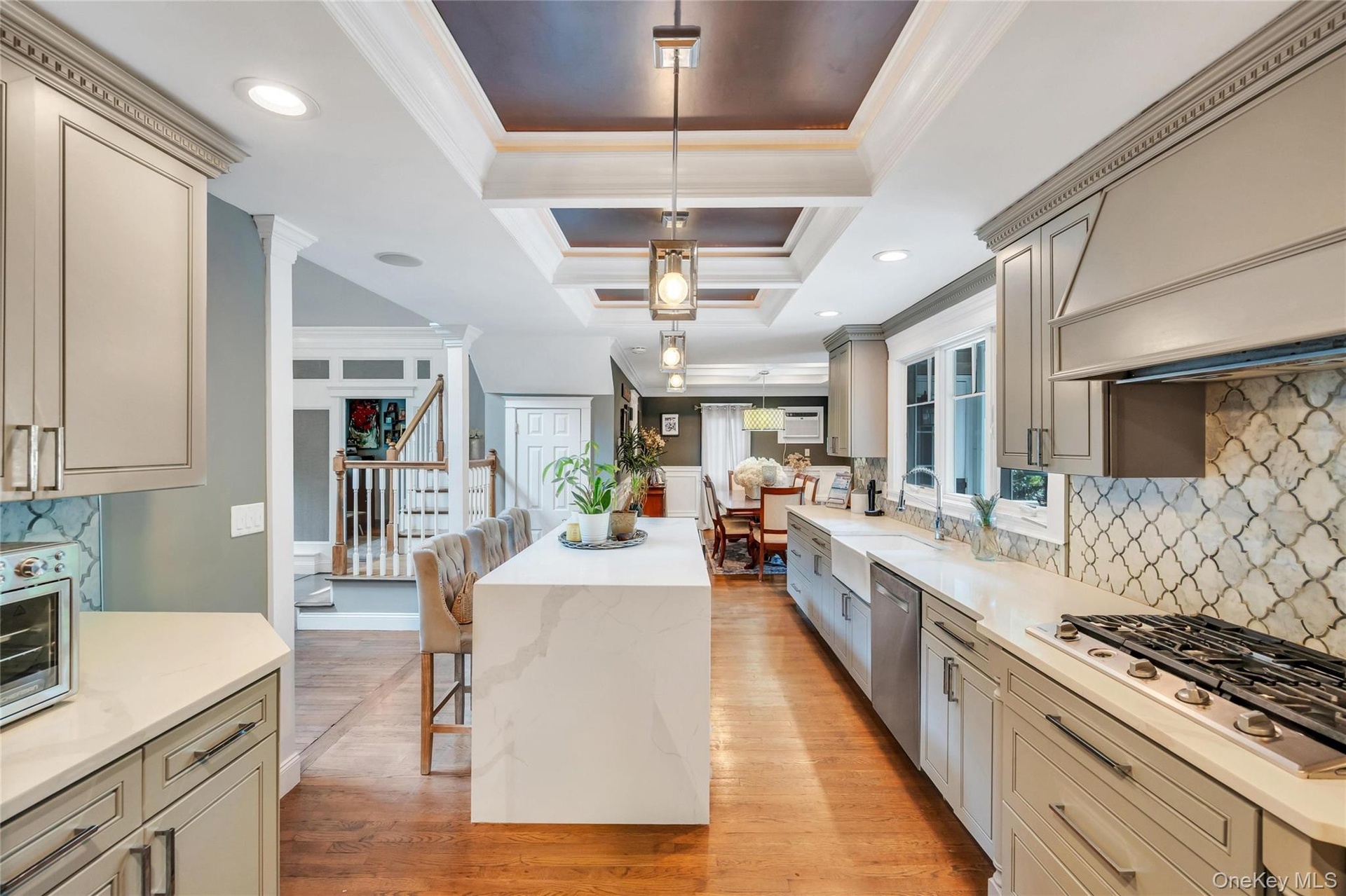 Gourmet kitchen with a waterfall edge island, recessed lighting, coffered ceiling detail, gas range, and geometric tile backsplash