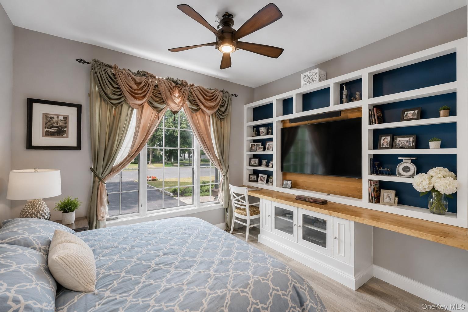 Room featuring a large window with draped valances, a ceiling fan with integrated lighting, and wood-finish flooring