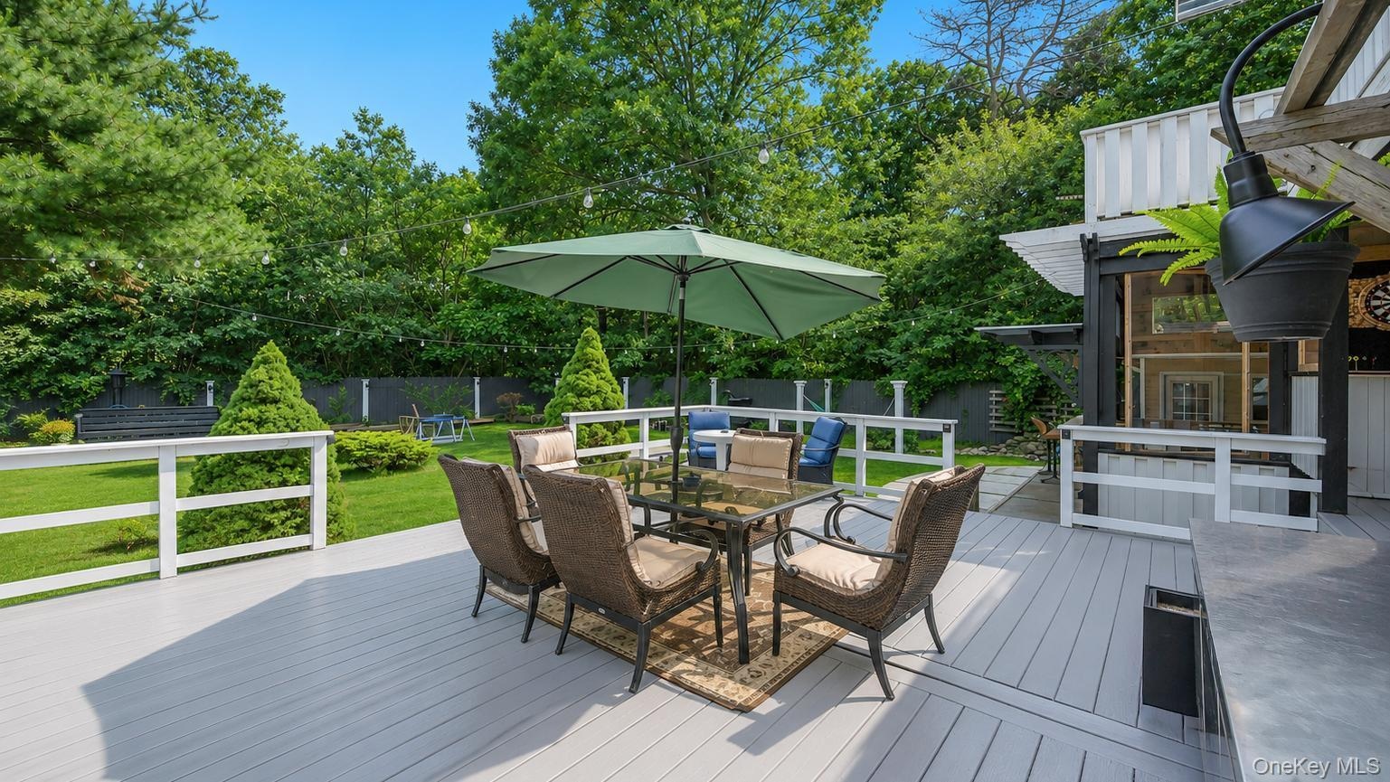 Expansive light-gray decking with white railings, featuring a glass-top dining table with wicker chairs