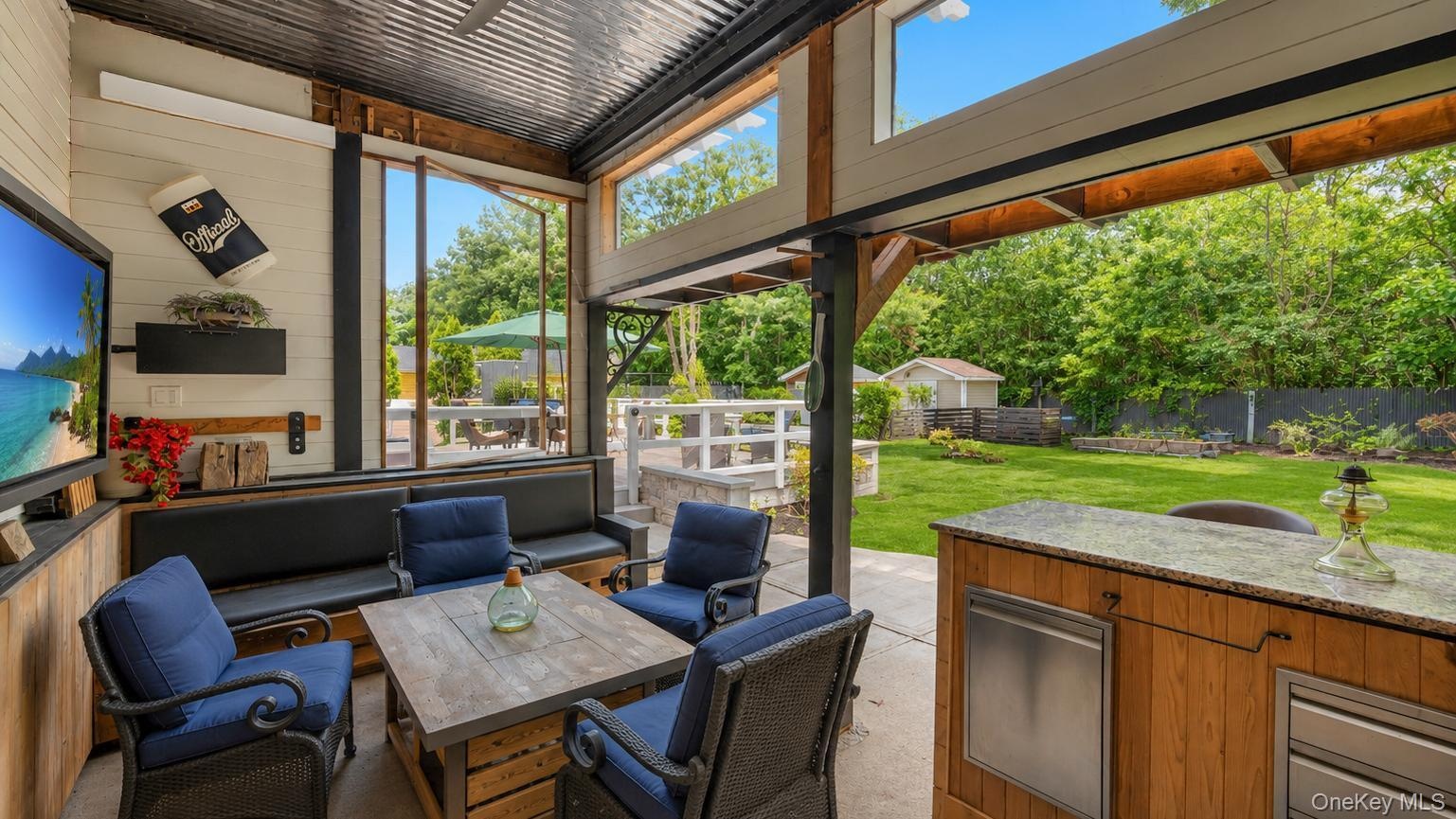 Outdoor entertainment area featuring a corrugated metal roof, wood shake bar with a stone countertop, built-in media console with television, exterior