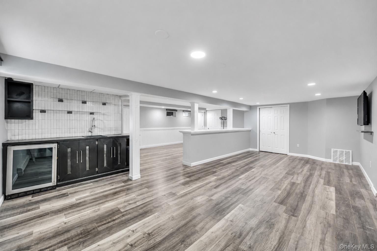 Spacious lower level featuring wood-finish flooring, recessed lighting, and a built-in wet bar with a beverage refrigerator