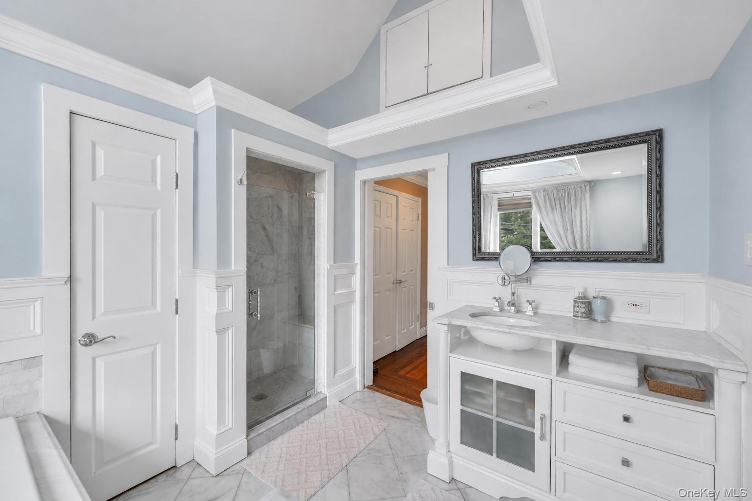 Bathroom featuring a glass-enclosed shower, white vanity with an undermount sink, marble-finish countertop, and decorative mirror
