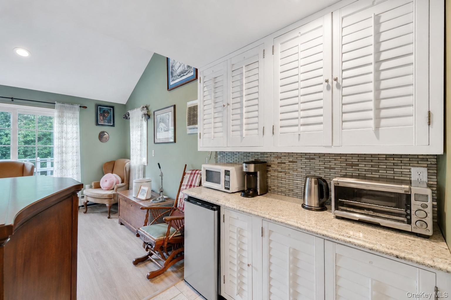 Galley area featuring white shaker-style cabinetry with louvered doors, a mosaic tile backsplash, and a granite-finish countertop