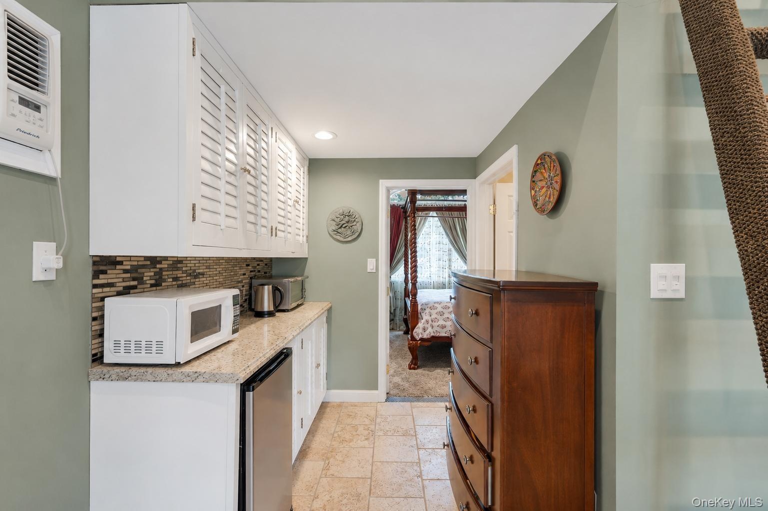 Galley area featuring white shaker-style cabinetry with louvered doors, a mosaic tile backsplash, and a granite-finish countertop