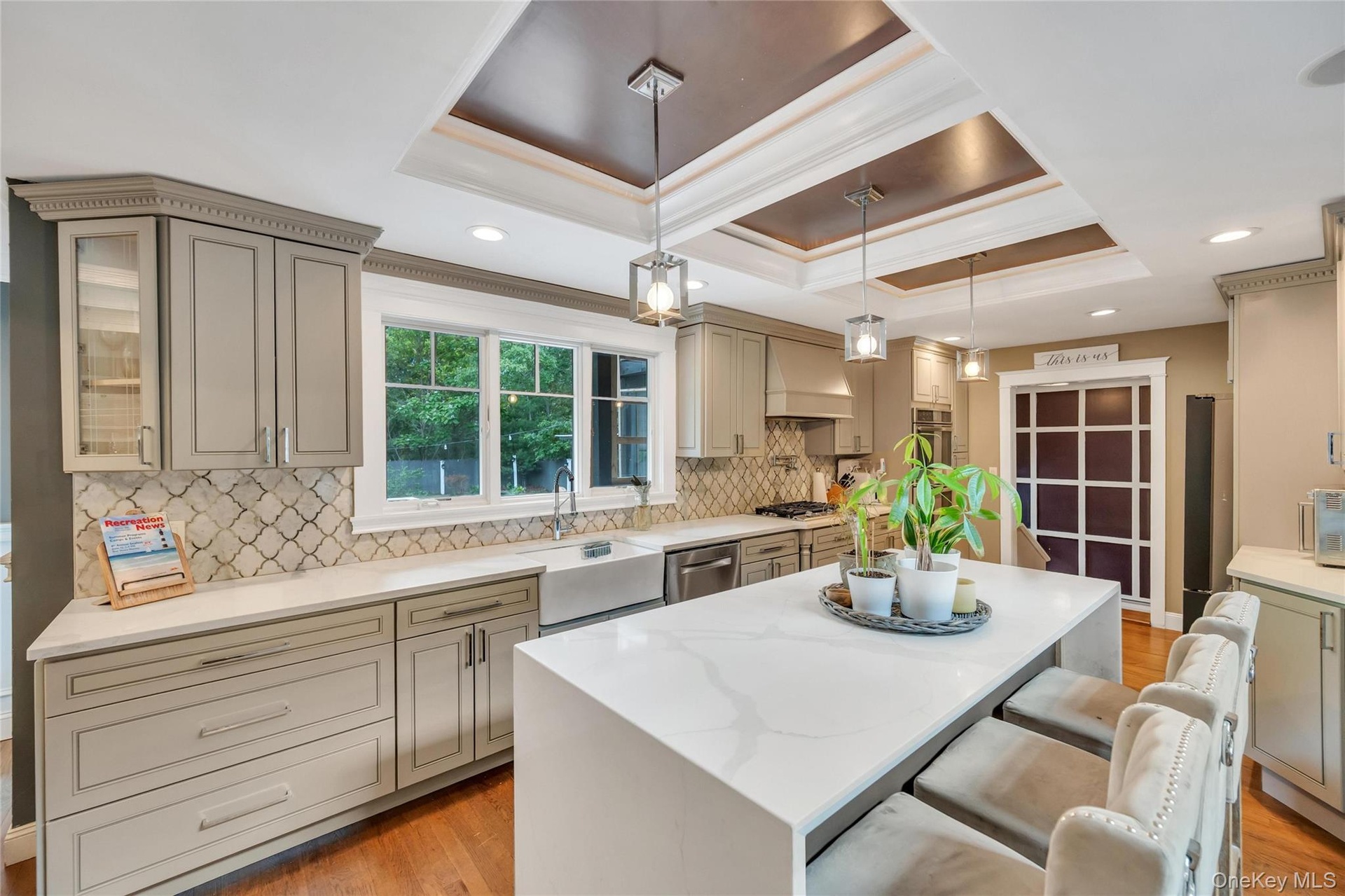 Expansive kitchen featuring a large central island with seating, a deep farmhouse-style sink, a patterned tile backsplash, and recessed and pendant li
