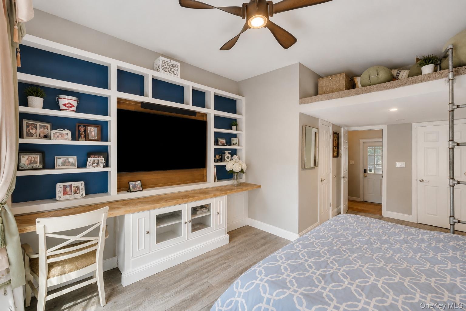 Custom built-in shelving with integrated media center, wood-finish flooring, recessed lighting, and a ceiling fan with light fixture