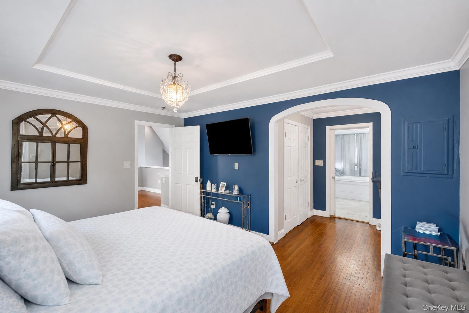 Bedroom featuring wood-finish flooring, a tray ceiling, and crown molding