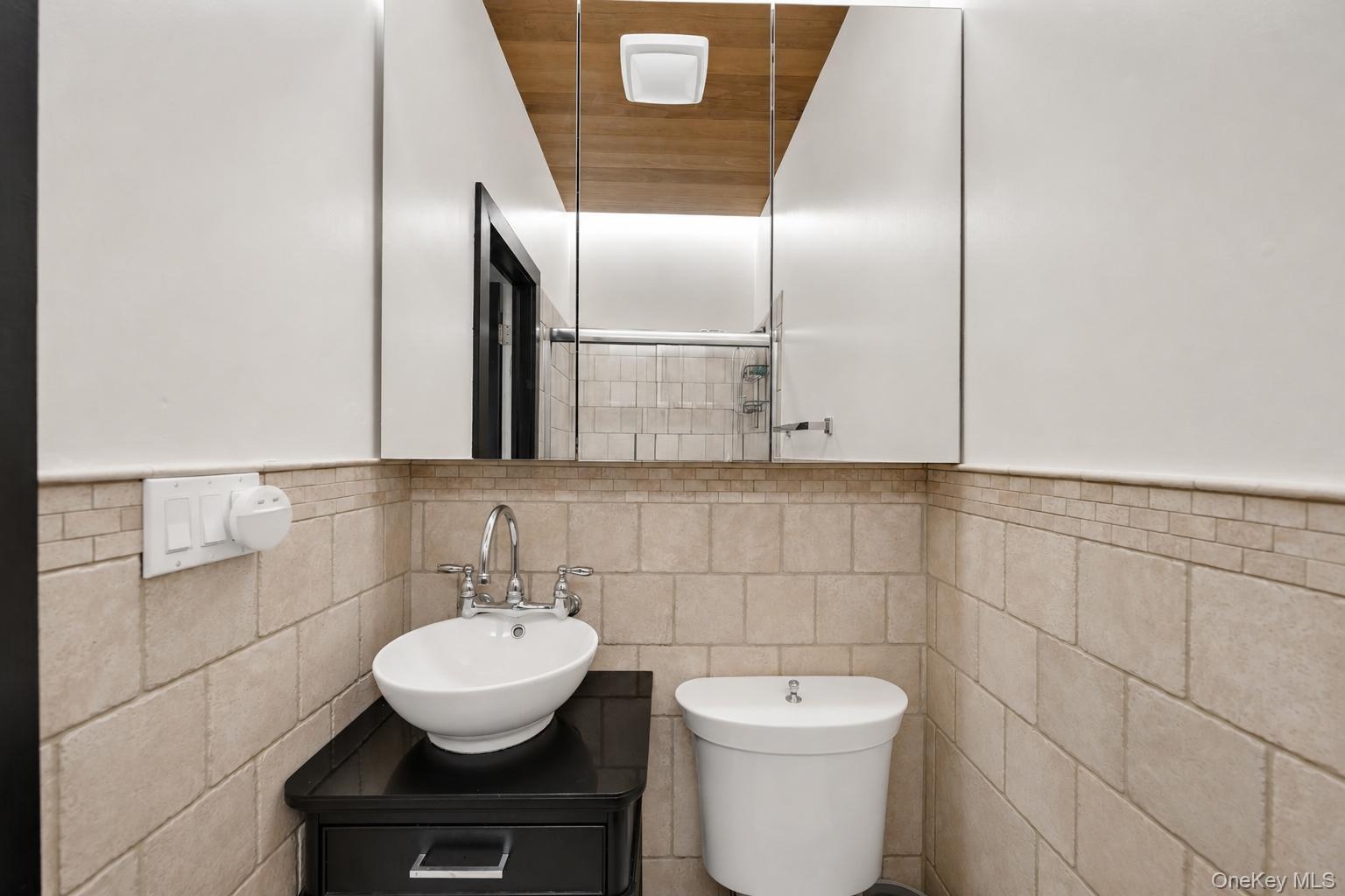Bathroom featuring a vessel sink with chrome fixtures, a dark wood-finish vanity with drawer, and light-toned tiled walls with decorative banding