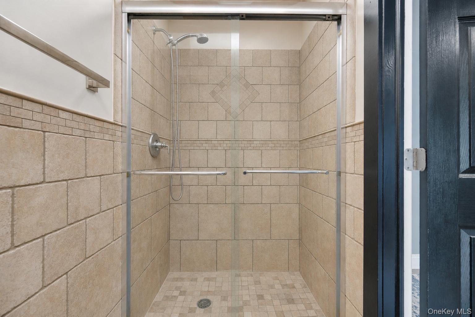 Tiled shower stall featuring clear glass enclosure with brushed nickel hardware, a decorative wall tile band, and a matching tiled shower pan