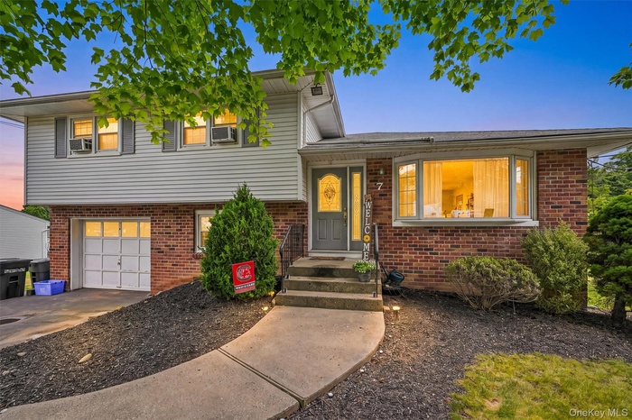 Split-level residence featuring a brick facade with light-colored siding, an attached garage, a bay window, and a concrete walkway leading to the main