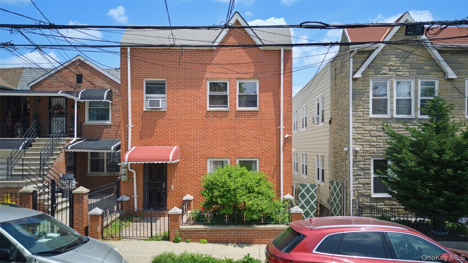 Brick facade with a gabled roofline, featuring a red fabric awning over the entry